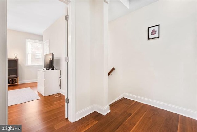 corridor featuring wood finished floors, an upstairs landing, and baseboards