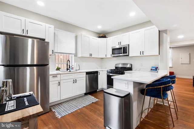 kitchen featuring a sink, white cabinetry, stainless steel appliances, a breakfast bar area, and dark wood-style flooring