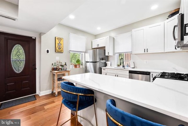 kitchen with light wood-style flooring, a peninsula, a kitchen breakfast bar, stainless steel appliances, and a sink