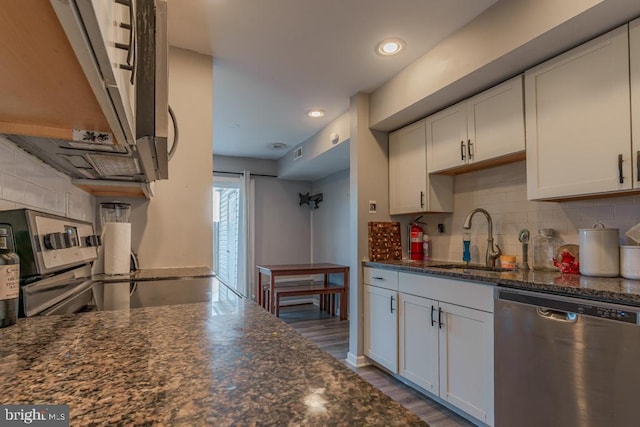 kitchen featuring dark stone counters, a sink, stainless steel appliances, white cabinets, and backsplash