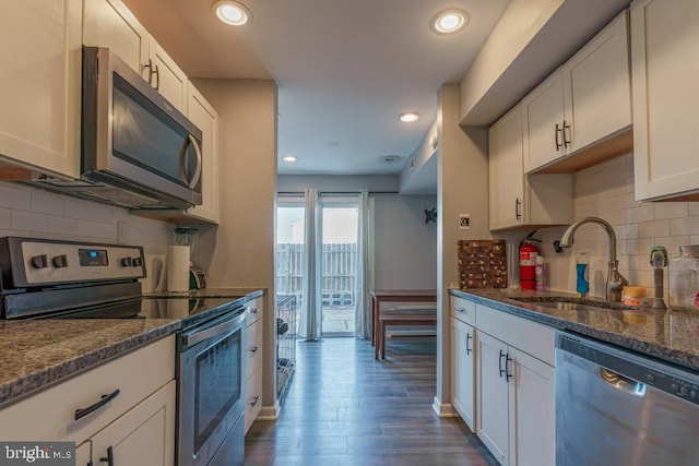 kitchen with dark wood finished floors, dark stone counters, stainless steel appliances, white cabinetry, and a sink