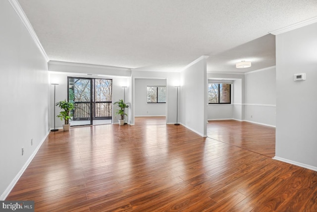 empty room with baseboards, a textured ceiling, wood finished floors, and crown molding