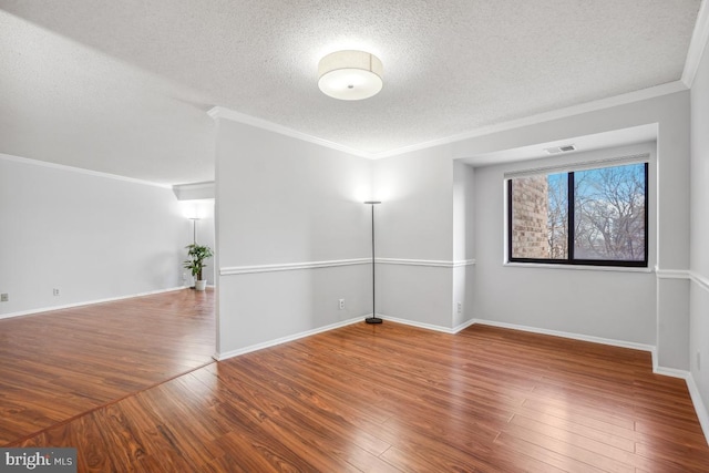 spare room with a textured ceiling, crown molding, baseboards, and wood finished floors