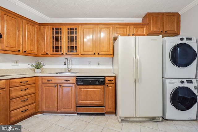 kitchen featuring stacked washer and dryer, paneled dishwasher, brown cabinets, freestanding refrigerator, and a sink