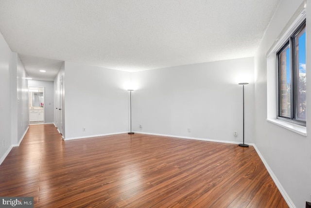 empty room featuring a textured ceiling, baseboards, and wood finished floors