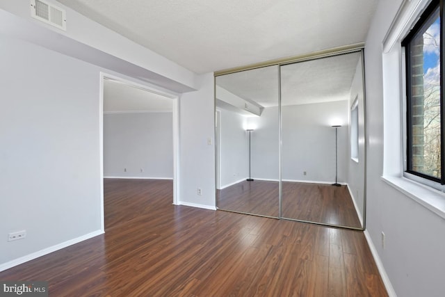 unfurnished bedroom featuring visible vents, baseboards, a closet, and wood finished floors