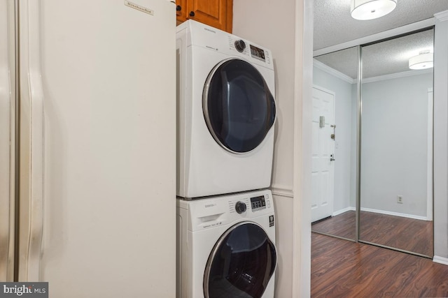 laundry area with wood finished floors, baseboards, ornamental molding, stacked washer and clothes dryer, and a textured ceiling