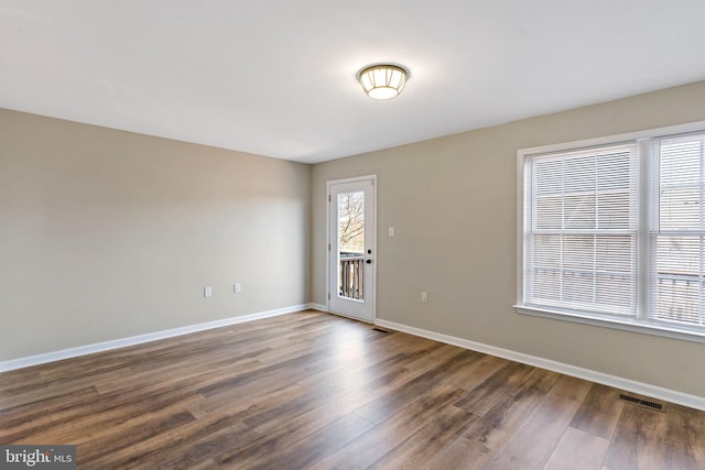 empty room featuring dark wood-style floors, visible vents, and baseboards