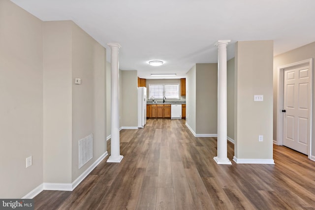 corridor featuring decorative columns, dark wood-style floors, visible vents, and baseboards