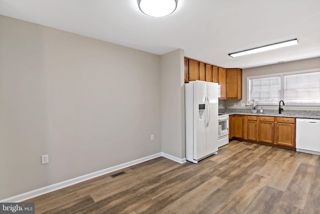 kitchen with white appliances, wood finished floors, baseboards, visible vents, and brown cabinets