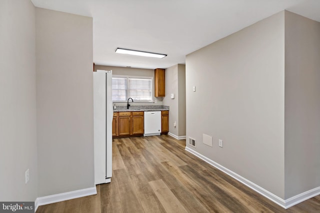 kitchen with visible vents, a sink, wood finished floors, white appliances, and baseboards