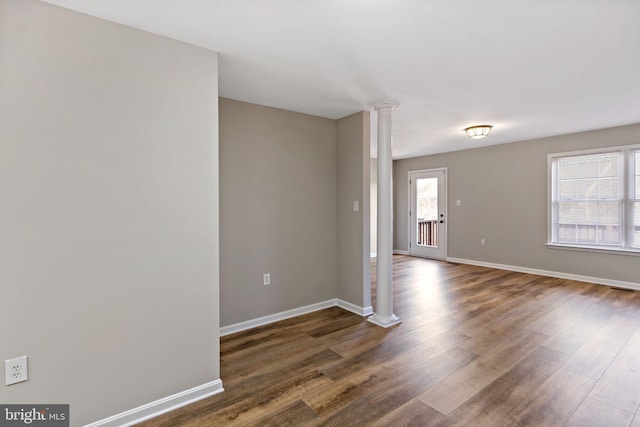 spare room with dark wood-type flooring, decorative columns, and baseboards