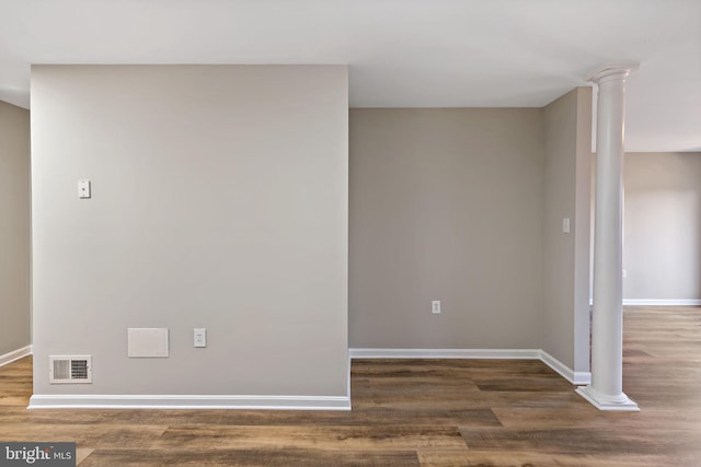 empty room with decorative columns, wood finished floors, visible vents, and baseboards