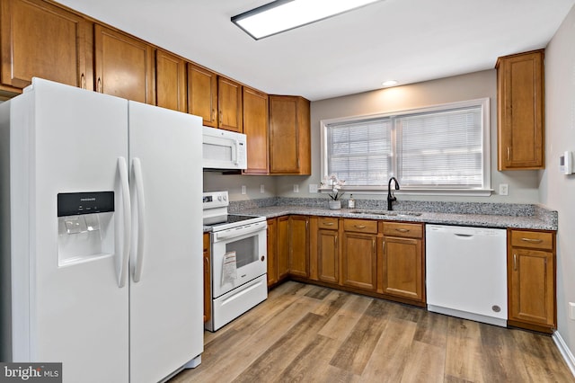 kitchen featuring white appliances, light wood-type flooring, brown cabinets, and a sink