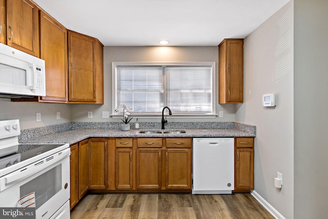 kitchen with a sink, wood finished floors, white appliances, brown cabinetry, and light stone countertops