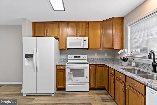 kitchen featuring brown cabinets, white appliances, light wood-type flooring, and a sink