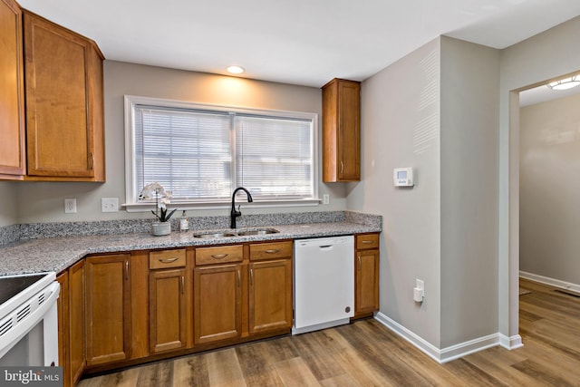 kitchen featuring a sink, white appliances, wood finished floors, and brown cabinetry