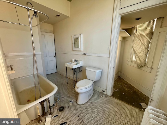 full bath featuring tile patterned flooring, a soaking tub, toilet, and baseboards