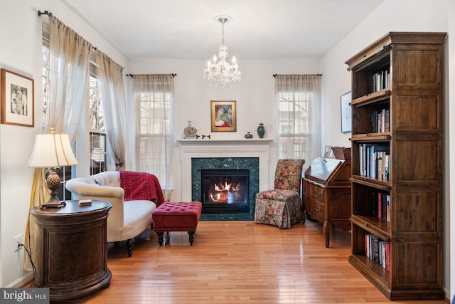 living area with light wood-type flooring, a notable chandelier, a healthy amount of sunlight, and a premium fireplace