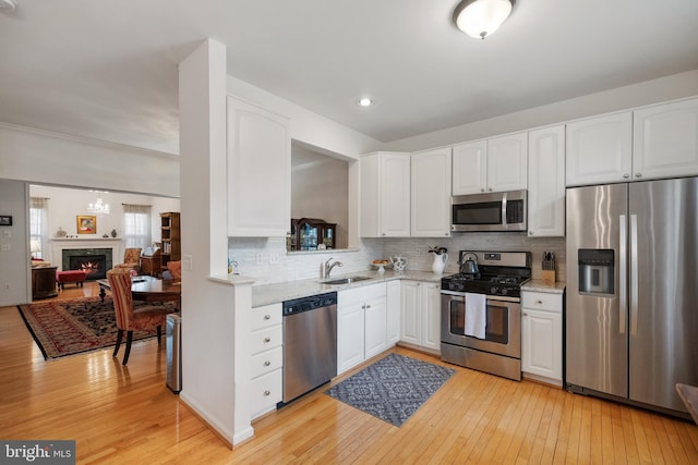 kitchen featuring light wood finished floors, decorative backsplash, appliances with stainless steel finishes, white cabinets, and a sink