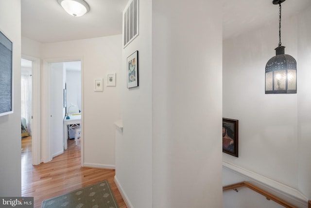 hall with wood finished floors, visible vents, and baseboards