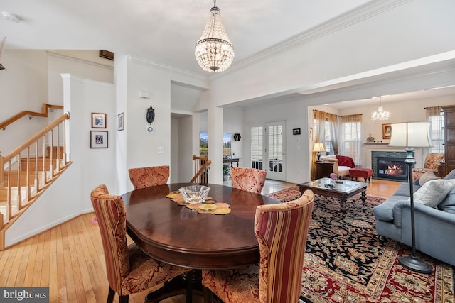 dining area featuring stairway, a fireplace, light wood-type flooring, and an inviting chandelier