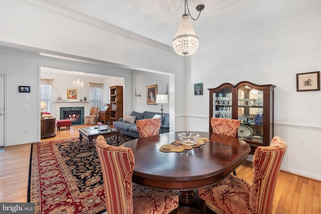 dining room featuring light wood-style flooring, ornamental molding, and a high end fireplace