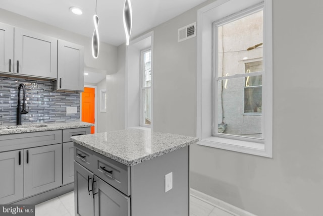 kitchen with visible vents, gray cabinetry, a sink, light stone counters, and backsplash