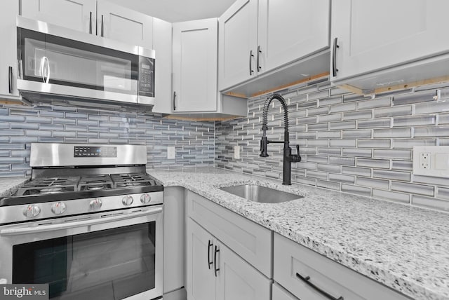 kitchen with light stone countertops, a sink, appliances with stainless steel finishes, white cabinetry, and backsplash