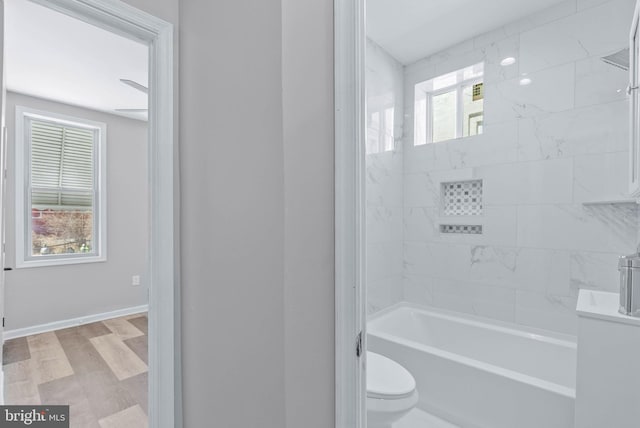 bathroom with tub / shower combination, toilet, wood finished floors, and baseboards