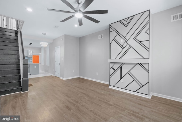 unfurnished living room featuring stairway, baseboards, wood finished floors, and ceiling fan with notable chandelier