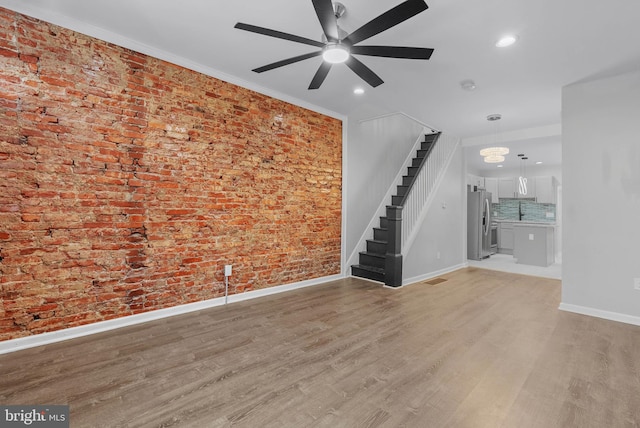 spare room featuring light wood-type flooring, baseboards, brick wall, and stairs