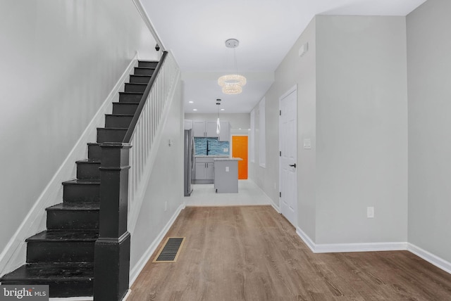 entryway with visible vents, baseboards, stairs, light wood-type flooring, and an inviting chandelier