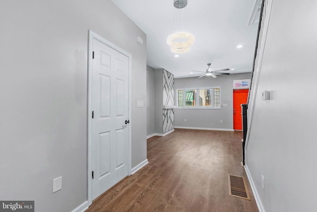 hallway with visible vents, baseboards, wood finished floors, and a chandelier