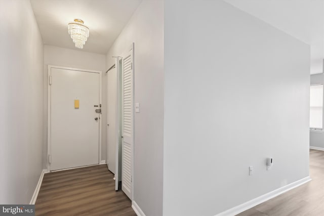 corridor featuring a chandelier, baseboards, and wood finished floors