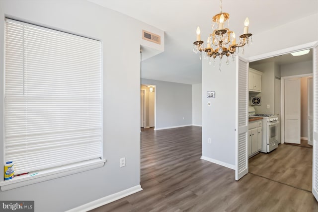 unfurnished dining area with wood finished floors, a notable chandelier, baseboards, and visible vents