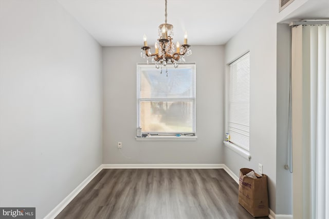 unfurnished dining area with baseboards, an inviting chandelier, and wood finished floors