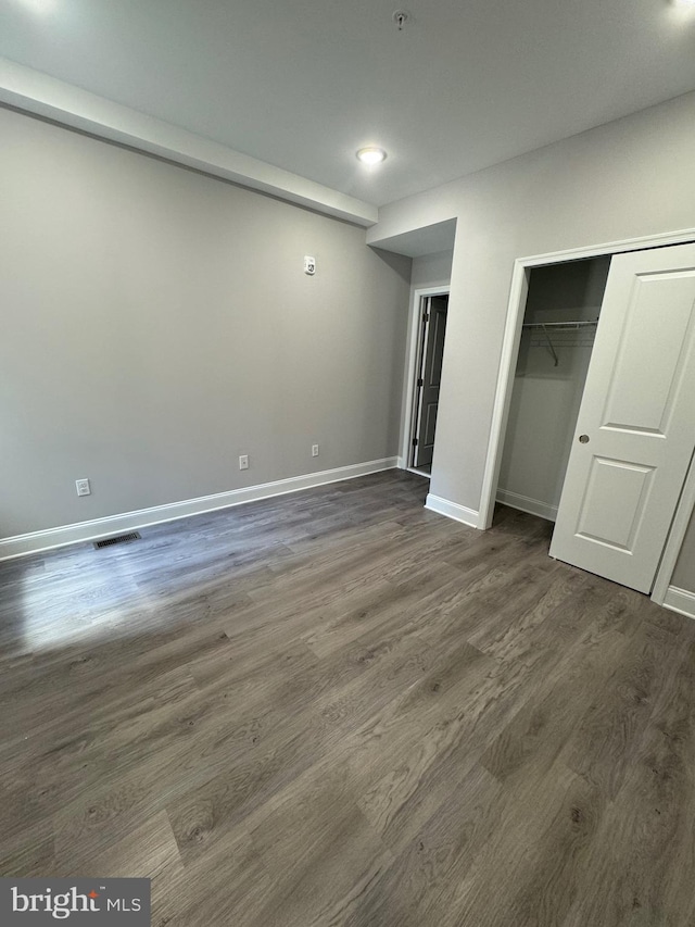 unfurnished bedroom with dark wood-type flooring, visible vents, baseboards, and a closet