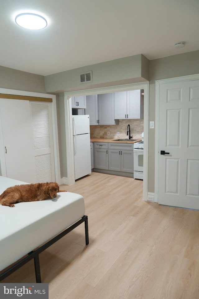 kitchen with tasteful backsplash, visible vents, light wood-style flooring, white appliances, and a sink