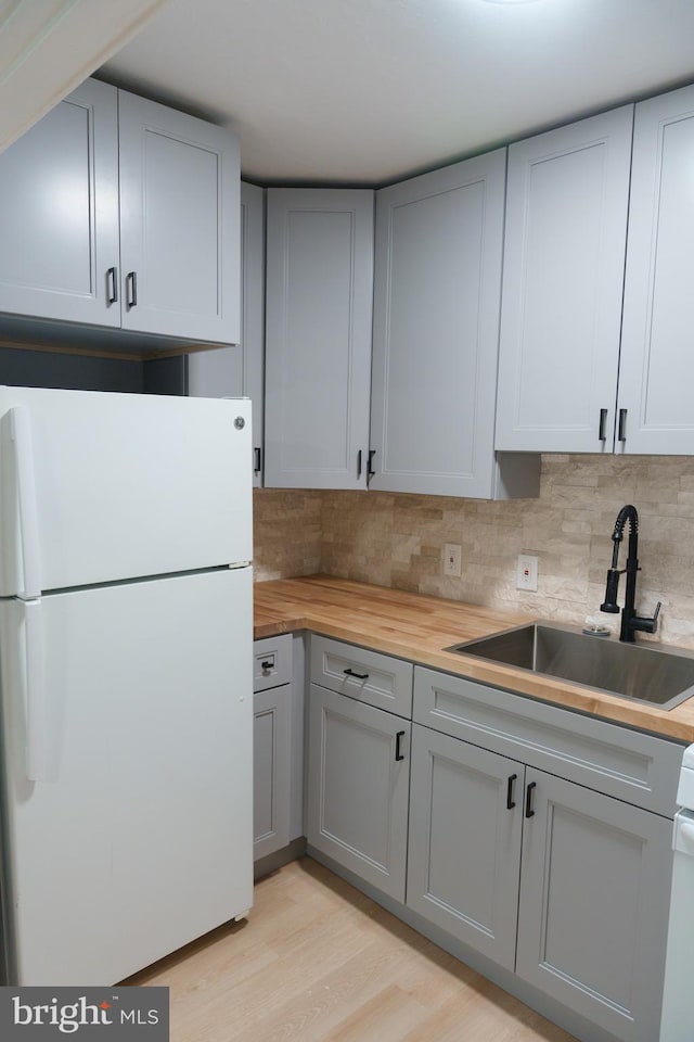 kitchen featuring wood counters, gray cabinetry, freestanding refrigerator, and a sink