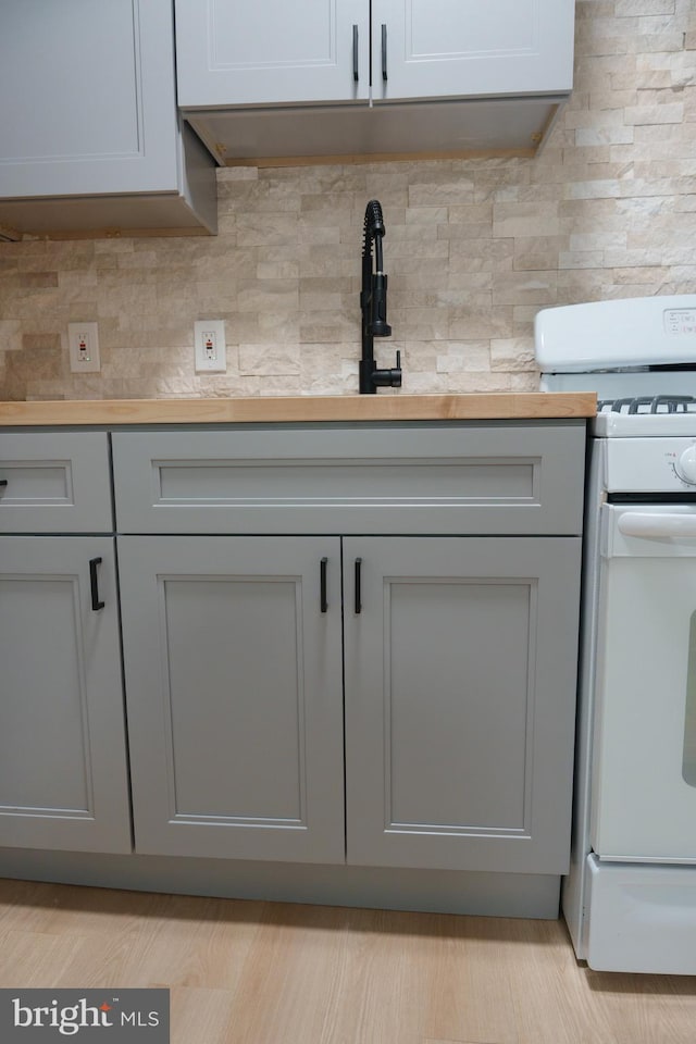 room details with tasteful backsplash, white gas stove, gray cabinets, and light countertops