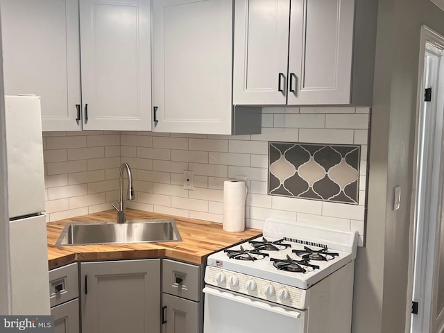 kitchen with white appliances, a sink, butcher block countertops, white cabinets, and backsplash