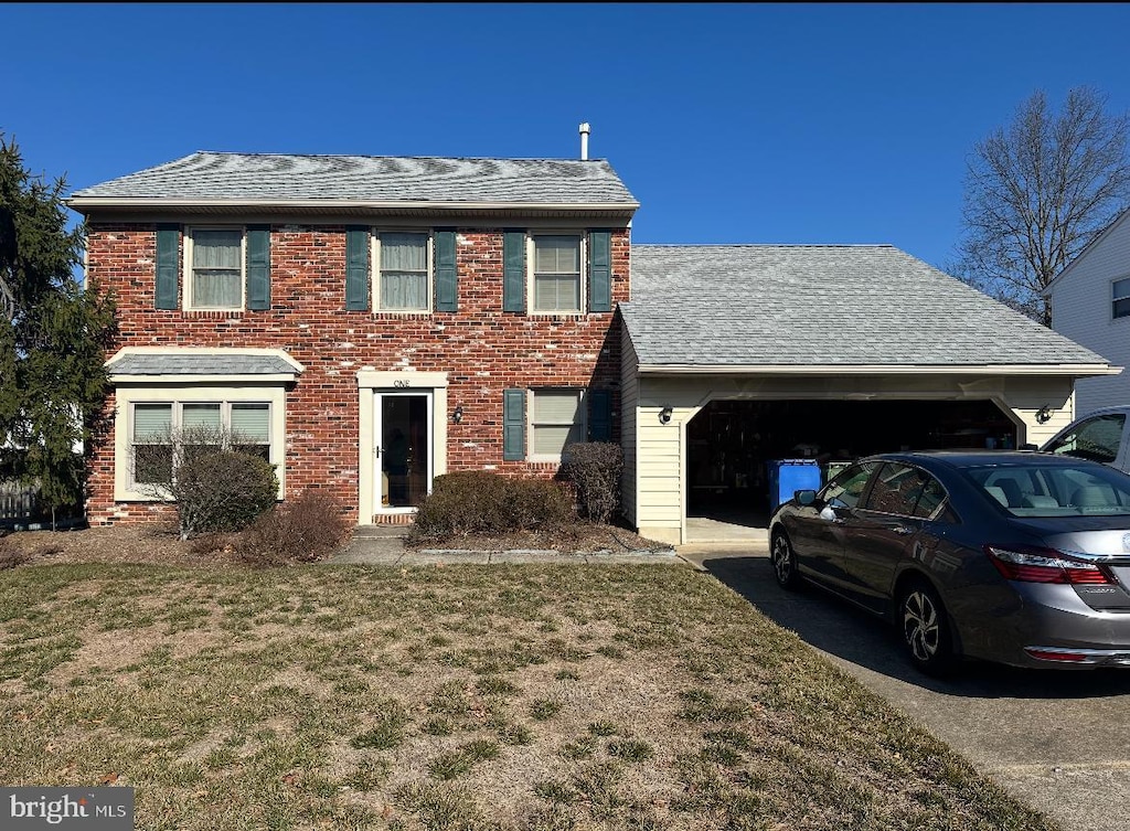 colonial inspired home featuring a front lawn, an attached garage, brick siding, and driveway