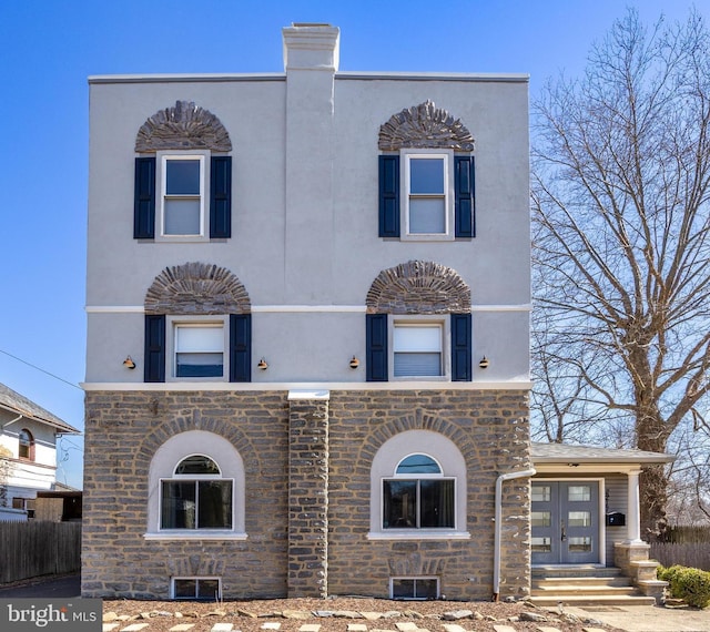 view of front of property featuring stone siding, stucco siding, and fence