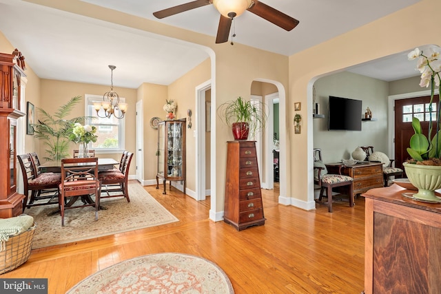 dining space featuring light wood-type flooring, arched walkways, baseboards, and ceiling fan with notable chandelier