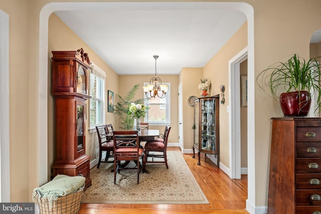 dining room with baseboards, a notable chandelier, arched walkways, and light wood finished floors