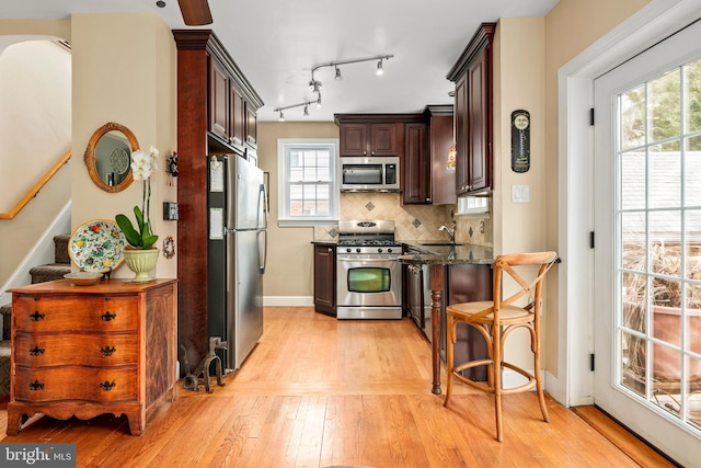 kitchen featuring light wood-type flooring, dark stone countertops, tasteful backsplash, stainless steel appliances, and dark brown cabinets