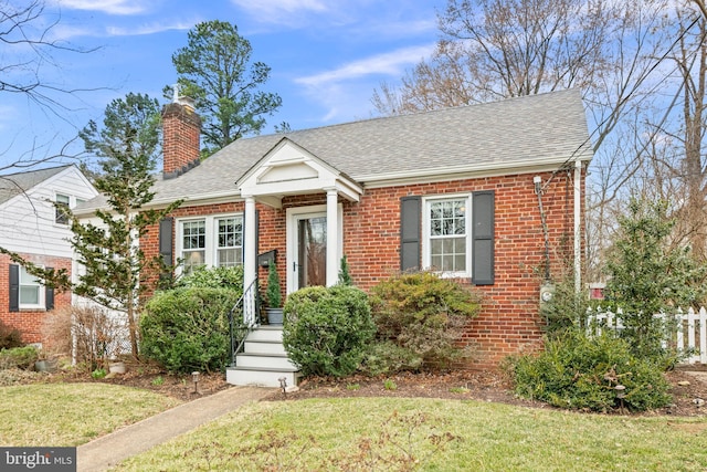 view of front facade featuring brick siding, a chimney, a front lawn, and a shingled roof