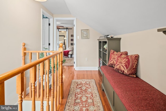 hallway featuring an upstairs landing, baseboards, lofted ceiling, and light wood-style floors