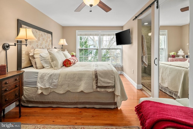 bedroom with a barn door, baseboards, wood finished floors, and a ceiling fan